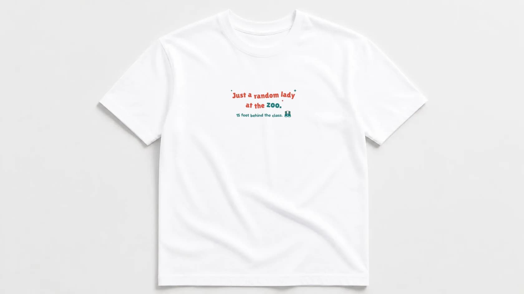 White unisex tee laid flat with "Just a random lady at the zoo. 15 feet behind the class." in bouncy coral and teal lettering with binoculars