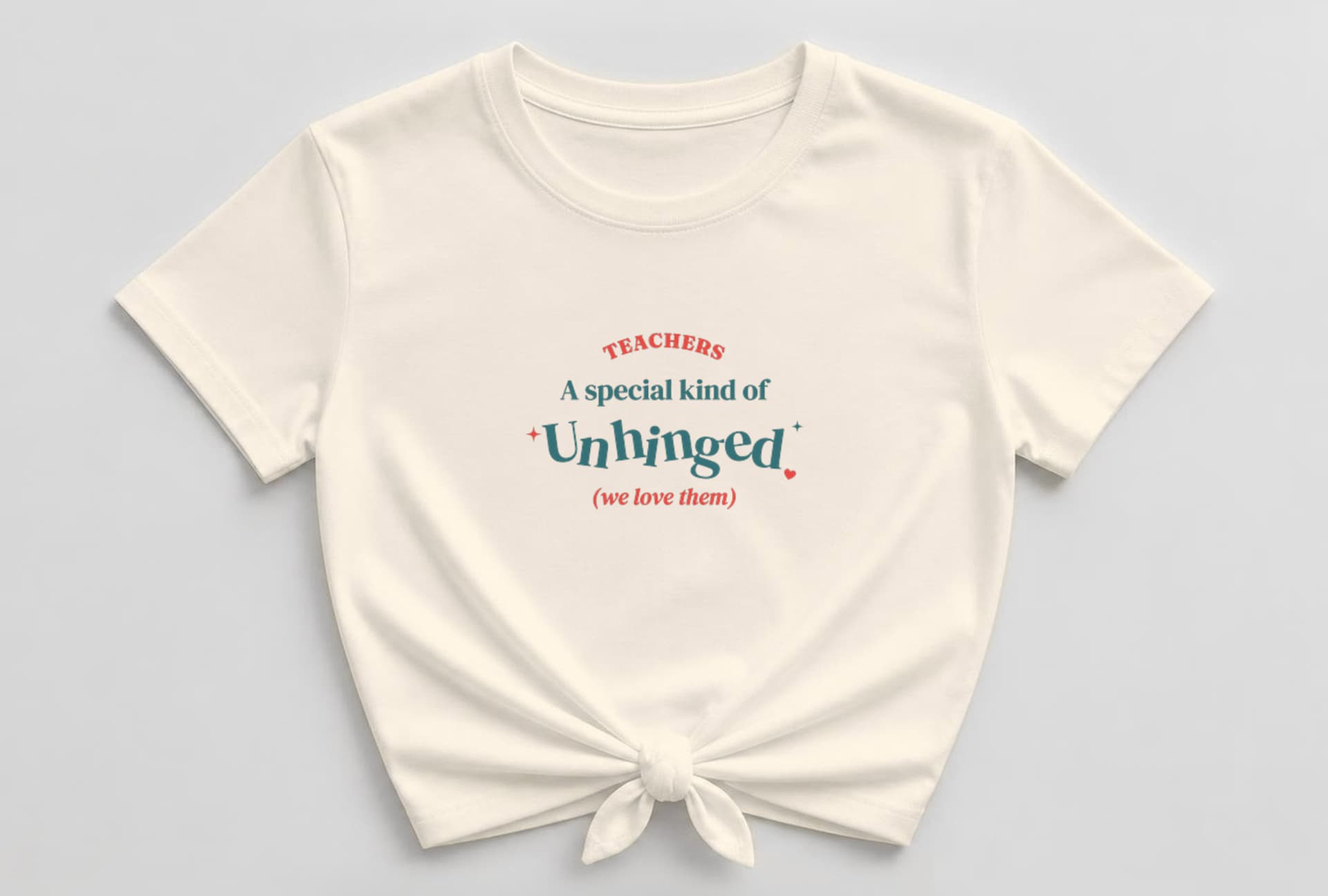 Soft cream knotted women's shirt with TEACHERS arched in coral-red capitals above "A special kind of" in teal, a big bouncy teal "Unhinged" with sparkles and a coral heart, and "(we love them)" in coral italic