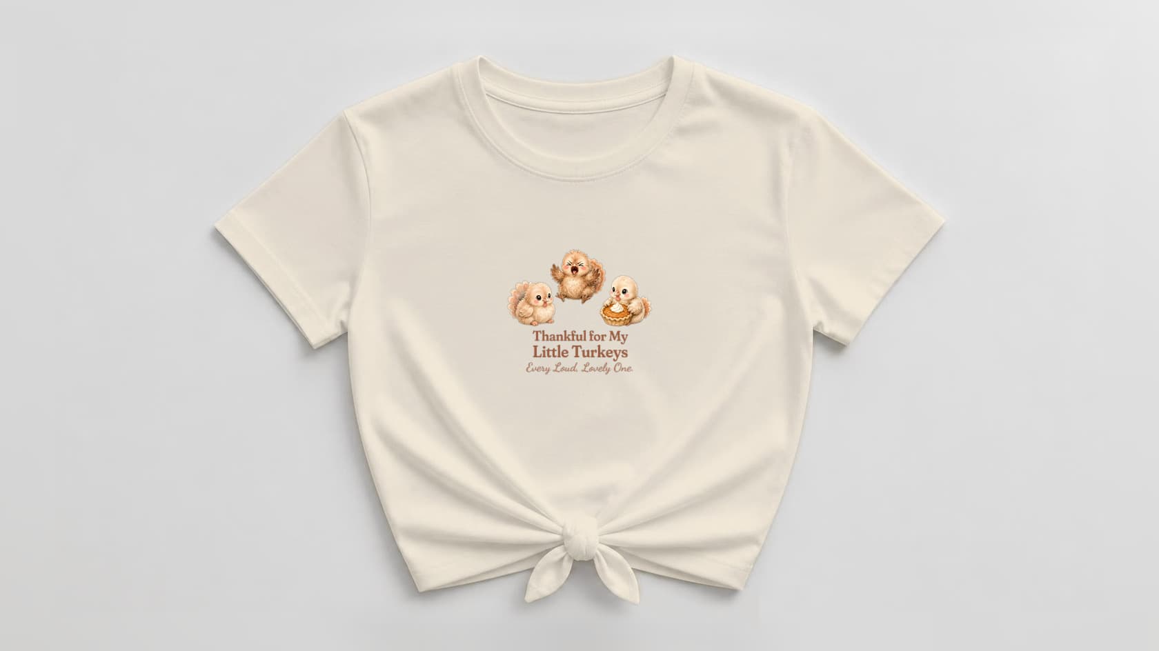 Natural cream knotted women's tee with gentle watercolor turkey chicks and a pumpkin pie, above "Thankful for My Little Turkeys. Every Loud, Lovely One." in warm brown serif and rust script