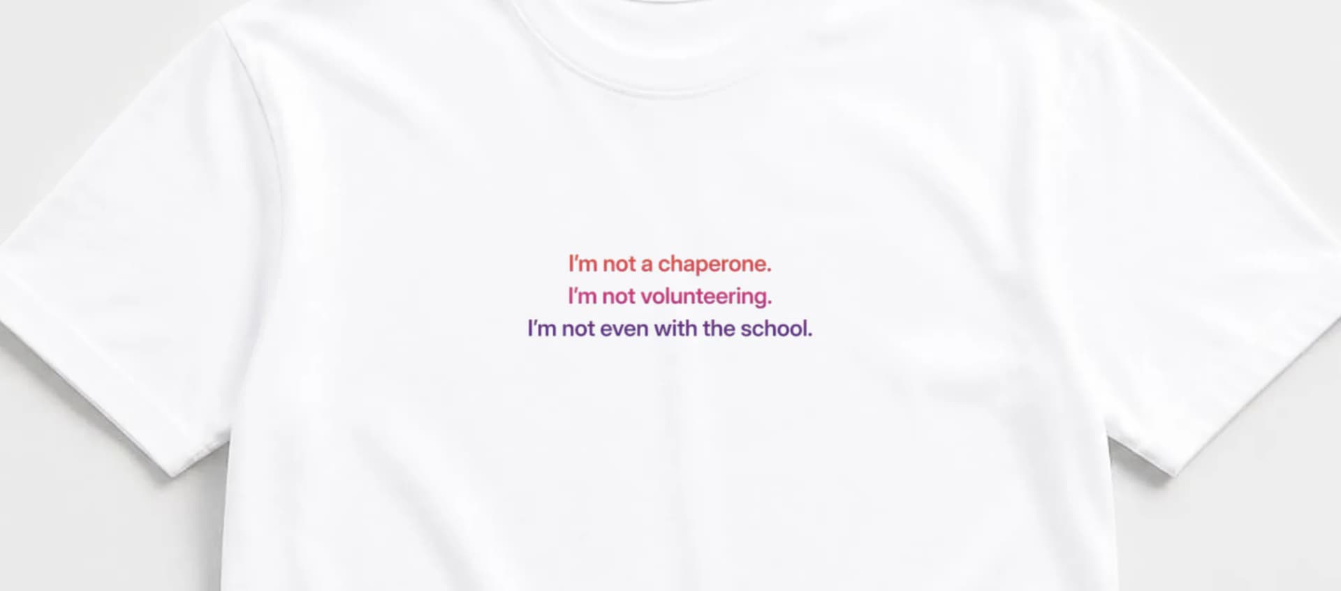 Close-up of white tee with "I'm not a chaperone. I'm not volunteering. I'm not even with the school." in coral-to-purple ombre lettering