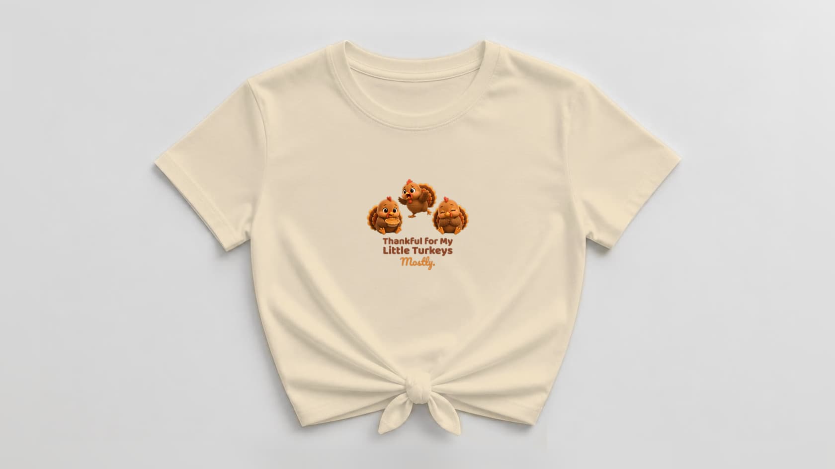 Soft cream knotted women's tee with three fluffy plush turkeys, the middle one yelling mid-tantrum, and "Thankful for My Little Turkeys. Mostly." in chocolate brown and orange lettering