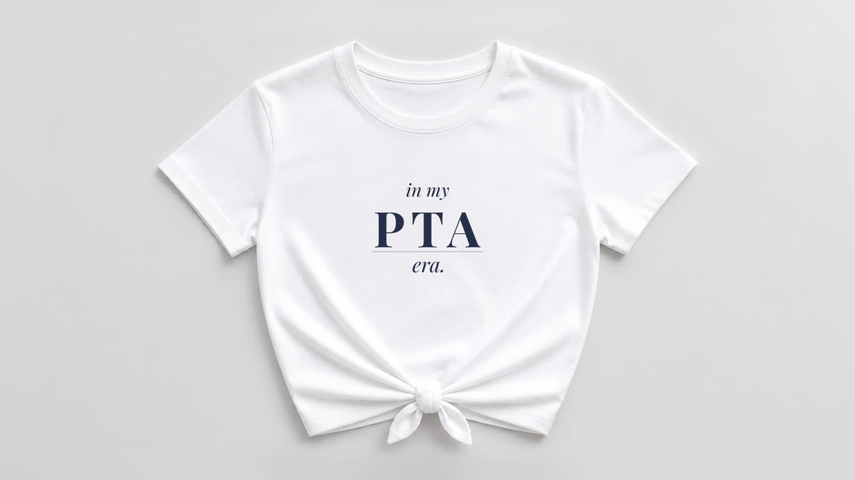 White knotted women's tee printed with "in my PTA era." in navy serif lettering