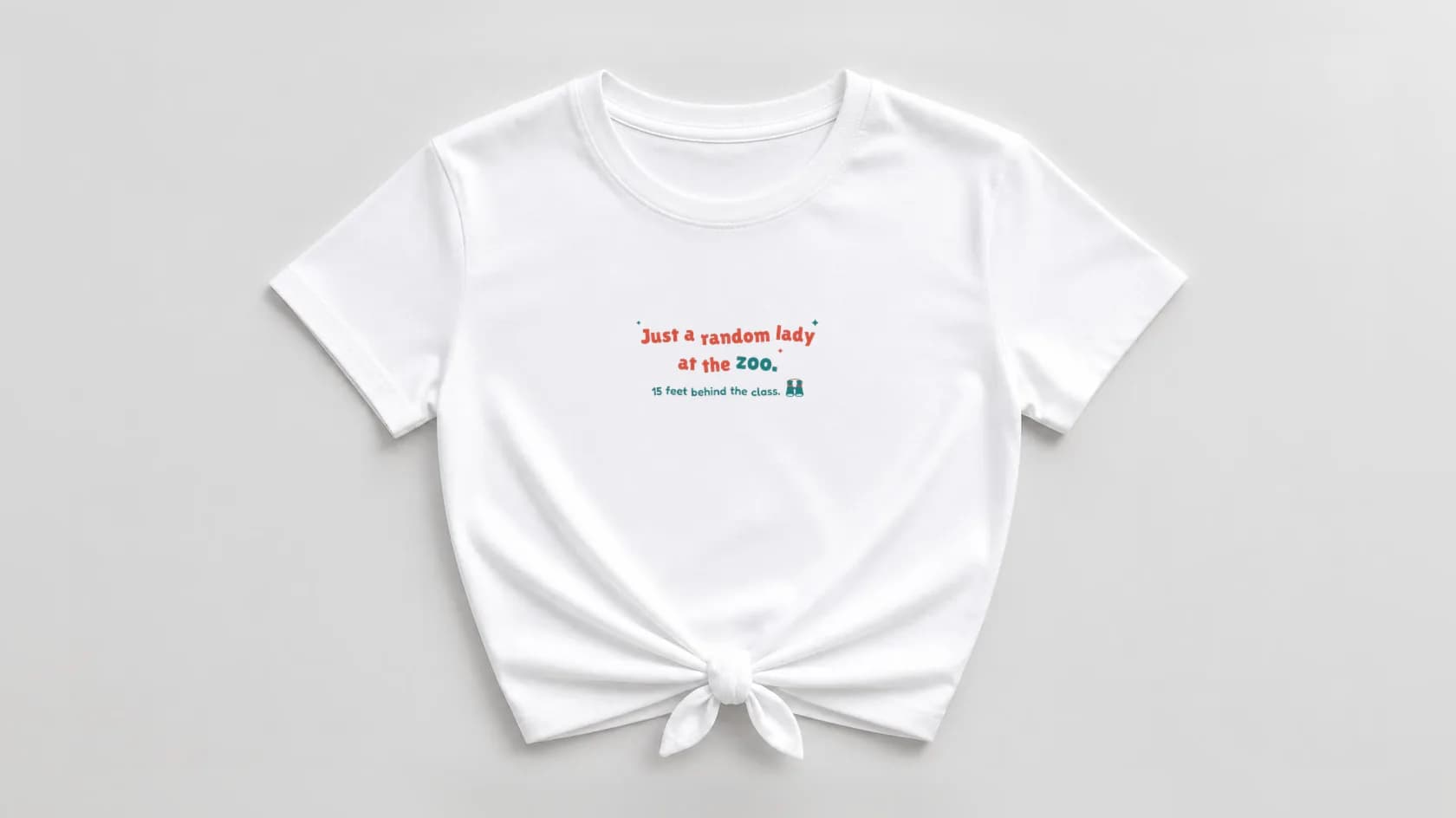 White knotted women's shirt with "Just a random lady at the zoo." in bouncy coral and teal and "15 feet behind the class." with a little pair of binoculars