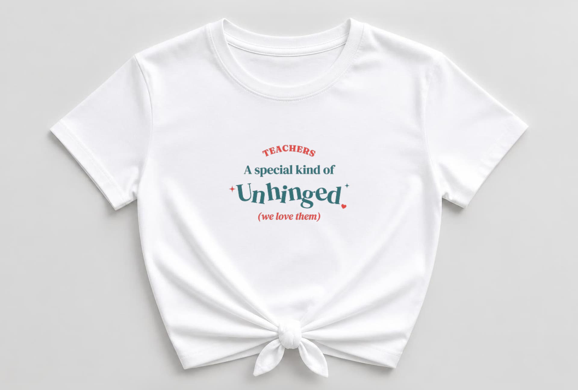 White knotted women's shirt with TEACHERS arched in coral-red capitals above "A special kind of" in teal, a big bouncy teal "Unhinged" with coral and teal sparkles and a coral heart, and "(we love them)" in coral italic