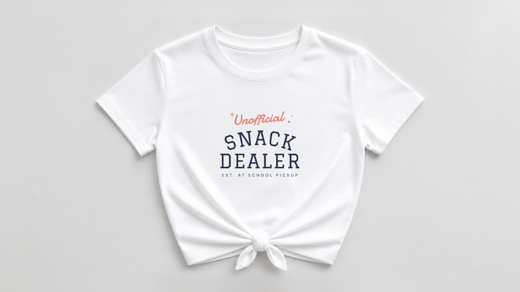 White knotted women's tee printed with "Unofficial Snack Dealer, est. at school pickup" in navy and coral lettering