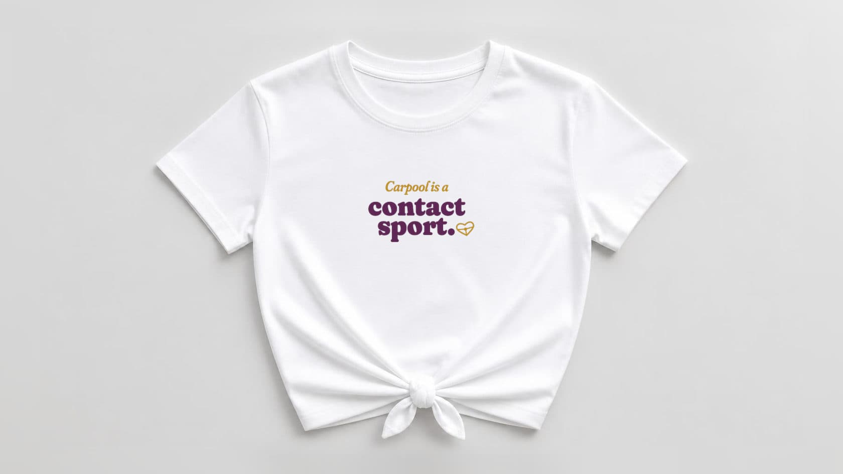 White knotted women's shirt with "Carpool is a" in mustard italic serif, "contact sport." in bold plum 70s soft serif, and a small mustard heart-shaped steering wheel